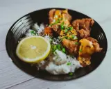 Chrupiące karaage z ryżem, posypane sezamem i szczypiorkiem, podane z plasterkiem cytryny.