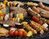 Una parrillada de que es bbq: brochetas de pollo y verduras, salchichas, bistecs y mazorcas de maíz asándose en una parrilla.