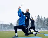 Athletik Training Fußball: Trainer korrigiert Ausfallschritt eines Spielers auf Kunstrasen. Zwei weitere Spieler machen Übungen im Hintergrund.