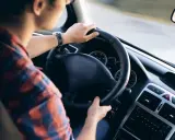 Mężczyzna w kratę prowadzi auto, kluczyki wiszą przy kierownicy. Czy AC przechodzi na nowego właściciela?