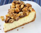 Kawałek sernika snickers z polewą karmelową i orzeszkami ziemnymi.