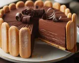 Une délicieuse charlotte au chocolat, ornée de biscuits à la cuillère et de copeaux de chocolat, est servie sur une assiette blanche.