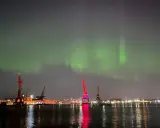 Norrsken över Göteborgs hamn. Kranar lyser upp natten medan himlen dansar i grönt.