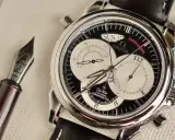 Elegante cronografo rattrapante Omega De Ville con quadrante nero e contatori argentati, accanto a una penna stilografica.