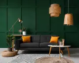 Canapé gris avec coussins orange vif sur fond vert foncé. Le jaune moutarde est une couleur qui va avec le vert foncé, créant un contraste chaleureux.