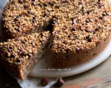 Una deliziosa torta di nocciole, ricoperta di granella di nocciole e gocce di cioccolato, con una fetta tagliata.