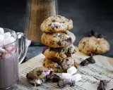 Un cookie chamallow fondant, empilé avec d'autres, à côté d'une tasse de chocolat chaud garnie de guimauves.