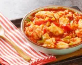 Un tazón de bacalao ajoarriero con pimientos y tomate, servido con una cuchara de madera sobre una servilleta a rayas.