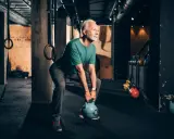Älterer Mann macht Stabi-Training mit Kettlebell im Fitnessstudio.
