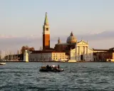 Le campanile et l'église de San Giorgio Maggiore à Venise se reflètent sur l'eau. Un bateau transporte des passagers.