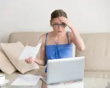Zmartwiona kobieta z okularami sprawdza dokumenty na laptopie, martwiąc się o przedawnienie długu za czynsz mieszkaniowy.