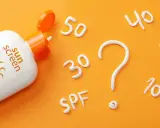 Flacon de crème solaire SPF 50 ouvert, avec des chiffres (30, 40, 20, 10) et un point d'interrogation formés en crème. Quel indice choisir ?