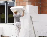 Budowlaniec montuje płyty ze styropianu grafitowego na elewacji. To dobry wybór, jaki styropian na elewację dla lepszej izolacji.