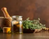 Olio essenziale timo proprietà: un flacone di vetro con olio dorato, un mortaio di legno e rametti di timo fresco.
