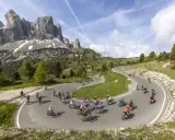 Ciclisti affrontano tornanti in una spettacolare salita alpe d'Huez, con maestose montagne sullo sfondo.