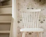 En vit pinnstol står framför en blommig tapet. Bredvid stolen syns en trappa. Kanske är det dags att måla pinnstolar?