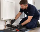 Instalator wykonuje wymianę grzejnika w bloku bez spuszczania wody, używając specjalistycznego sprzętu.