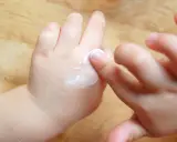 Mani di bambino applicano crema, un gesto che aiuta a contrastare la pelle atopica, alleviando secchezza e prurito.