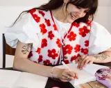 Une jeune femme souriante fait une dédicace livre, stylo à la main, devant un cahier ouvert et un paquet cadeau violet.