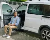 Hombre sonriente sentado en un asiento elevador de coche, listo para salir. Un ejemplo de soluciones de movilidad accesibles.