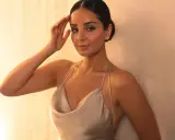 Elegante Frau mit festlichen Frisuren, die ein seidiges Kleid trägt und sich an eine Wand lehnt.