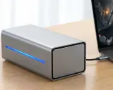 Srebrna obudowa egpu do laptopa z niebieskim podświetleniem, podłączona do laptopa z grą na ekranie.