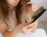 Donna preoccupata guarda i capelli persi sul pettine, chiedendosi perché perdo capelli.