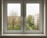 Ventana doble de PVC con vista a edificios y árboles. Cumple la normativa de ventanas para viviendas, ofreciendo aislamiento y seguridad.