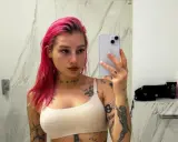 Młoda Leosia z kolorowymi włosami i licznymi tatuażami na ciele robi sobie selfie w łazience.