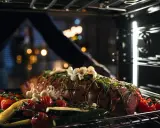 Ein Braten mit Kräutern, Knoblauch, Tomaten und Zucchini wird in den Ofen geschoben. So wird ein Dialoggarer zum Leben erweckt.