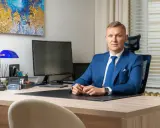 Mężczyzna w niebieskim garniturze siedzi przy biurku w nowoczesnym biurze.
