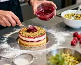 Un chef ajoute une touche finale à un gâteau, déposant une compotée pour créer un insert croustillant framboise.