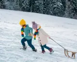 Dzieci w kolorowych szalikach ciągną sanki po ośnieżonym stoku. Idealny pomysł, gdzie w góry z dziećmi na zimową zabawę.