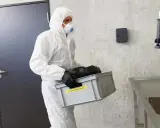 Hombre con traje blanco y mascarilla, lleva caja con equipo de protección obligatoria de vías respiratorias.