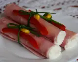 Roladki z szynki z chrzanem, ozdobione papryką i szczypiorkiem, prezentują się apetycznie na białym talerzu.