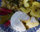 Częściowo roztopiony camembert z ziemniakami, ogórkami kiszonymi i rzodkiewką na talerzu.
