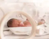 Maleńki wczesniak w inkubatorze, z rurką w nosku, śpi spokojnie.