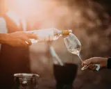 En person häller upp ett glas vin från en flaska. Solen skiner och skapar en varm atmosfär.