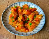 Krispiga bitar av sweet chili kyckling, toppade med sesamfrön och salladslök, serveras på en blårandig tallrik.