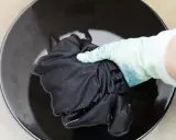 Mano con guante sumerge ropa blanca desteñida de negro en tinte oscuro.