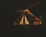Przytulny namiot na nocnym polu biwakowym, oświetlony od środka.