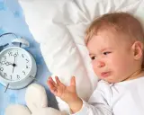 Płacz 1,5 rocznego dziecka, które nie chce spać w dzień. Obok budzik i pluszaki.