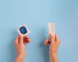 Manos sostienen un preservativo y pastillas anticonceptivas, mostrando opciones de planificación familiar.