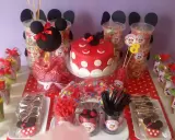 Mesa de fiesta temática de Minnie Mouse con pastel, galletas, palomitas y muchos centros de chuches para niños.