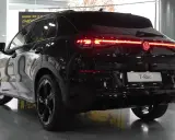 El Volkswagen T-Roc 2026 negro brillante, con sus luces traseras LED rojas encendidas, se exhibe en un concesionario.