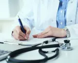 Lekarz analizuje wyniki badań, decydując, kiedy zwiększyć dawkę Euthyroxu. Na biurku stetoskop i laptop.