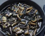 Calamares en su tinta, un plato oscuro y sabroso, servido en una sartén de hierro fundido.