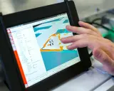Ein Finger tippt auf ein Tablet, das eine 3D-Ansicht mit einem Roboter zeigt. Die dji app windows wird zur Steuerung genutzt.