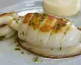 Delicioso sepia a la plancha con hierbas verdes, servido en un plato blanco con una guarnición cremosa.