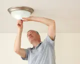 Mężczyzna wymienia żarówkę w lampie sufitowej. Prosty poradnik, jak wymienić żarówkę w suficie.